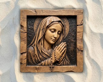 May include: A square wooden wall plaque featuring a relief carving of a woman with a head covering and a halo, shown with hands clasped in prayer while holding a rosary with a crucifix. The carving is set within a rustic, textured wood frame.