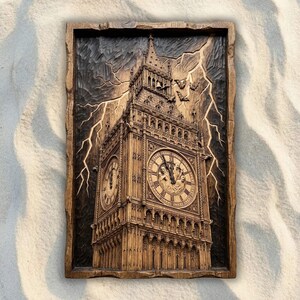 May include: A rectangular wooden wall plaque featuring a detailed relief carving of the Big Ben clock tower. The dark wood surface depicts the tower against a stormy sky with carved lightning bolts and several small bats in flight.