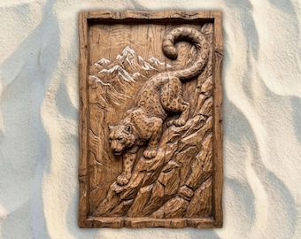 May include: A rectangular wooden wall art piece featuring a carved relief of a snow leopard climbing a rocky mountain. The leopard has a spotted coat and is set against a backdrop of snow-capped mountains.