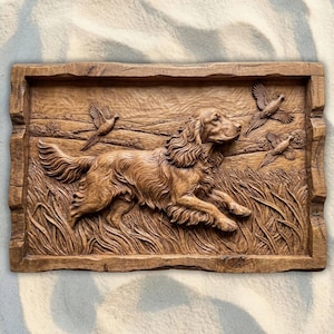 May include: A rectangular, wooden relief carving depicting a dog running through tall grass, with three birds flying above. The dog has long, flowing fur and is carved in detail. The frame has a rustic, textured edge.