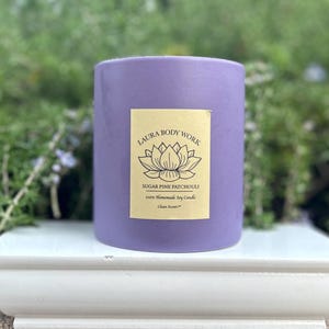 May include: Purple soy candle with a gold label that reads "Laura Body Work, Sugar Pine Patchouli, 14oz Homemade Soy Candle, Clean Scent". The label also features a lotus flower design.