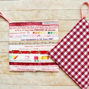 May include: Two pot holders, one with a red and white gingham pattern and the other with a patchwork design made from colorful fabric scraps. The patchwork pot holder has a pink fabric loop for hanging.