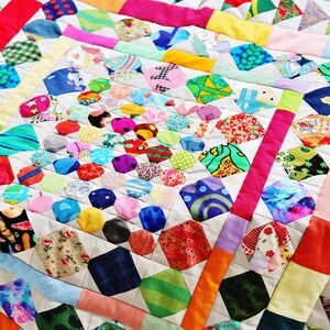 Könnte beinhalten: Ein farbenfrohes, handgefertigtes Quilt mit Patchwork-Design. Das Quilt zeigt eine Vielzahl von Stoffen in leuchtenden Farben, darunter Rot, Blau, Grün, Gelb und Rosa. Das Quilt besteht aus einer Kombination aus geometrischen Formen und Mustern.