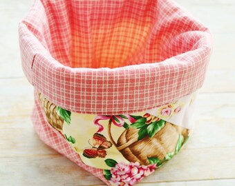 May include: A pink and white gingham fabric storage basket with a floral print on the bottom. The basket is empty and ready to be filled.