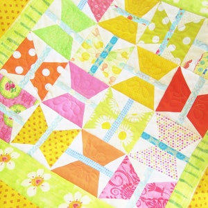 Op de afbeelding: Een kleurrijk quilt met een vlinderpatroon. De quilt is gemaakt van verschillende stoffen in tinten roze, geel, groen, oranje en blauw. De quilt is gestikt met een eenvoudig steekpatroon.