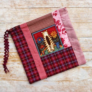 Puede incluir: Una bolsa con cremallera de patchwork rojo, rosa y blanco con un diseño de gato. El gato es marrón y blanco con un collar rojo y está rodeado de flores.