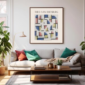 May include: A framed print of a geometric abstract art piece by Theo van Doesburg. The artwork features a white background with colorful squares, rectangles, and semi-circles in shades of blue, yellow, pink, and red. The print is hanging on a white wall in a living room setting.