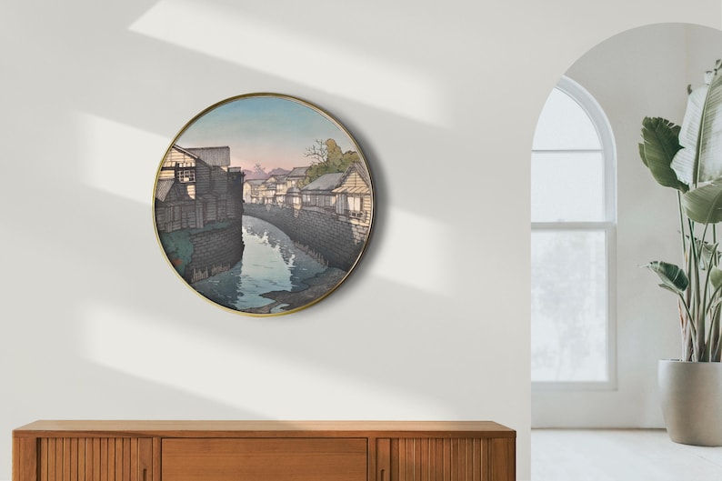 May include: A round wall art print featuring a Japanese woodblock print of a canal with buildings on either side. The print is in shades of gray, blue, and white.