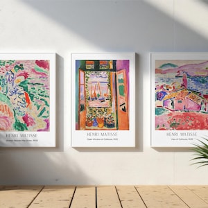 Op de afbeelding: Drie ingelijste Henri Matisse kunstprints. De prints tonen kleurrijke abstracte schilderijen met titels als "Woman Beside the Water", "Open Window at Collioure" en "View of Collioure". De lijsten zijn wit.