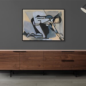 May include: A framed abstract painting with geometric shapes in shades of blue, black, and white on a beige background. The painting is hanging on a gray wall above a wooden cabinet with black metal legs.
