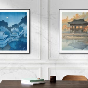 May include: Two framed Japanese woodblock prints. The print on the left depicts a blue and white scene of a traditional Japanese building with a moon in the sky. The print on the right shows a traditional Japanese building with a red roof and a reflection in the water.