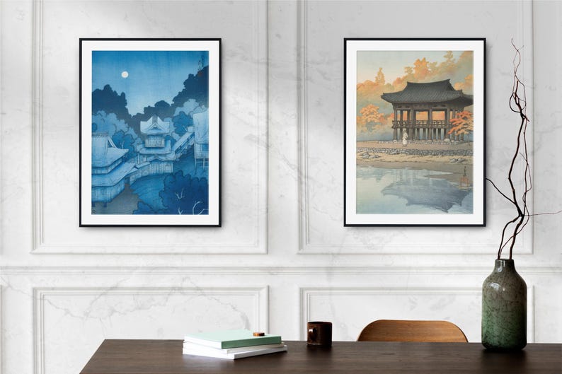 May include: Two framed Japanese woodblock prints. The print on the left depicts a blue and white scene of a traditional Japanese building with a moon in the sky. The print on the right shows a traditional Japanese building with a red roof and a reflection in the water.
