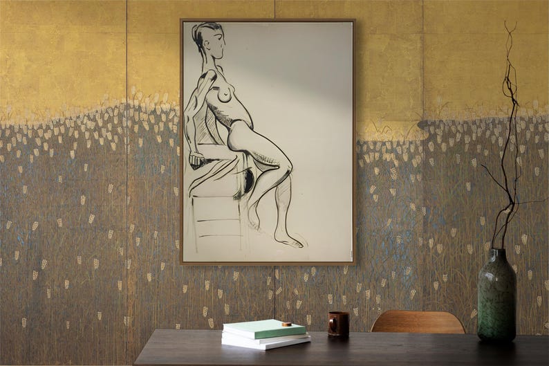 May include: A framed black and white line drawing of a nude figure sitting on a stool. The drawing is on a white background and is framed in a gold frame. The drawing is hanging on a wall with a gold and brown textured wallpaper.
