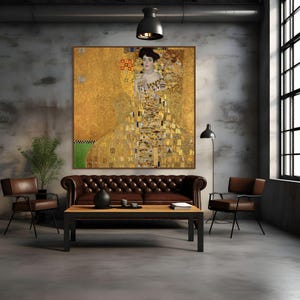 Puede incluir: Interior con una gran pintura enmarcada con fondo dorado y una mujer con vestido dorado. Un sofá de cuero marrón, dos sillas marrones y una mesa de centro negra están frente a la pintura. La habitación tiene suelo y paredes de hormigón.