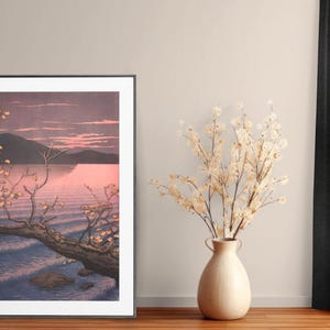 May include: A framed print of a Japanese-style landscape painting depicting a tree branch reaching over a body of water with a mountain in the background. The sky is a soft pink and purple.
