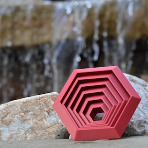 May include: A red geometric nesting tray with a concentric circle design. The tray is made of a smooth, hard plastic and has a glossy finish.