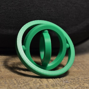 May include: A green plastic fidget toy with three interlocking rings. The rings can be spun and rotated.