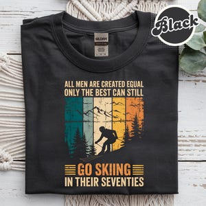 May include: Black t-shirt with a vintage ski design. The shirt features a skier on a mountain and the text: "ALL MEN ARE CREATED EQUAL ONLY THE BEST CAN STILL GO SKIING IN THEIR SEVENTIES."