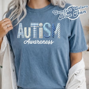Könnte beinhalten: Blaues T-Shirt mit dem Wort "AUTISMUS" in einer Mischung aus Mustern und Farben und "Awareness" in weißer Schrift. Das Shirt ist ein Comfort Colors Blue Jean. Das Bild zeigt eine Person, die das Shirt trägt.