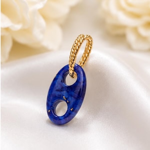 May include: A gold-toned hoop earring with a twisted rope texture, featuring a detachable oval-shaped pendant. The pendant is made of deep blue resin with embedded gold-colored flecks and two circular cutouts in the center of the oval form.