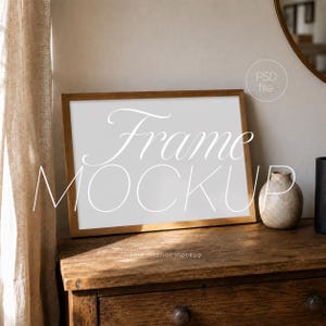 May include: A horizontal wooden picture frame mockup with a blank white center, featuring the text "Frame MOCKUP" and "PSD file" overlaid. The frame sits on a dark wooden surface next to a small, textured, light-colored ceramic vase.