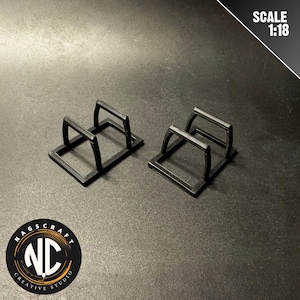Könnte beinhalten: Zwei schwarze, rechteckige Präsentationsständer mit griffartiger Struktur oben. Sie stehen nebeneinander auf einer dunklen Oberfläche. Der Text "SCALE 1:18" ist zu sehen.