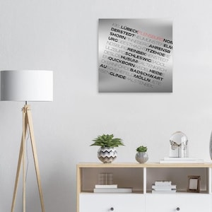 Puede incluir: Un fondo plateado con texto negro que enumera ciudades y pueblos alemanes. El texto está dispuesto en una columna vertical, comenzando con "Kiel" en la parte superior y terminando con "Halstenbek" en la parte inferior.