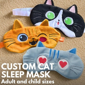 May include: Three cat-shaped sleep masks in black, orange, and blue. The black mask has white accents and green eyes. The orange mask has a winking expression. The blue mask has heart-shaped eyes. Text reads "CUSTOM CAT SLEEP MASK Adult and child sizes."