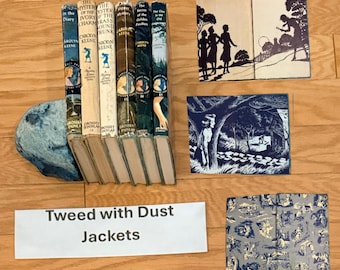 May include: A collection of vintage books with colorful dust jackets, including titles like "The Mystery of the Ivory Charm" and "The Clue in the Old Album." The books are propped up on a blue, textured bookend. A sign reads "Tweed with Dust Jackets."
