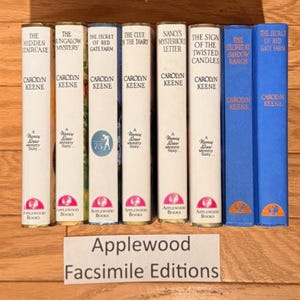 May include: A collection of Nancy Drew mystery books by Carolyn Keene. The book spines are white, blue, and green, with titles like "The Hidden Staircase" and "The Secret of Red Gate Farm." The books are from Applewood Books.