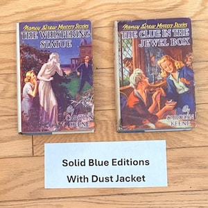 May include: Two vintage Nancy Drew mystery books, "The Whispering Statue" and "The Clue in the Jewel Box," with colorful cover illustrations. The books are from the "Solid Blue Editions" series and include dust jackets.