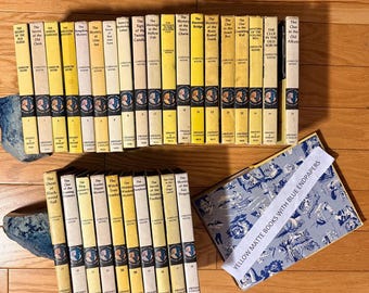May include: A collection of vintage yellow and off-white hardcover books, many with the title "The Clue" or "Mystery" on the spine. The books are arranged on a wooden surface, with a book open to show blue endpapers. A white label reads "YELLOW MATTE BOOKS WITH BLUE ENDPAPERS."