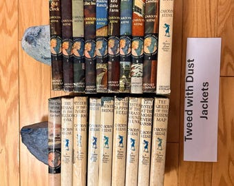 May include: A collection of nineteen Nancy Drew mystery books by Carolyn Keene, published by Grosset & Dunlap. The books feature various spine colors and titles, including The Secret of the Old Clock and The Quest of the Missing Map. A white card reads Tweed with Dust Jackets.
