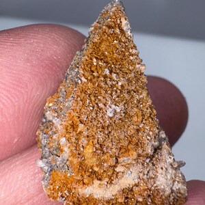May include: A small, triangular-shaped rock with a rough, textured surface. The rock is primarily brown with some white and gray areas. It appears to be a natural mineral specimen.