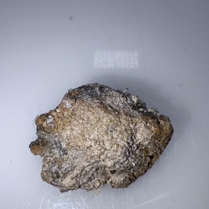 May include: A small, rough, gray and brown rock with a crystalline texture.