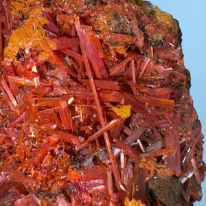 Könnte beinhalten: Nahaufnahme eines roten und orangefarbenen Mineralproben mit einer rauen, strukturierten Oberfläche. Das Mineral besteht aus vielen dünnen, nadelförmigen Kristallen.