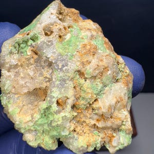 Puede incluir: Una roca rugosa de forma irregular con una superficie blanca y cristalina. La roca está cubierta de manchas verdes y marrones, lo que le da un aspecto moteado.