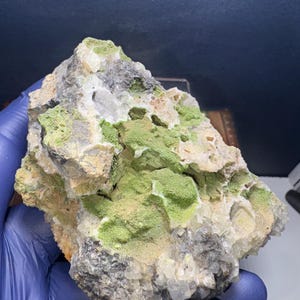 May include: A rough, gray rock with a cluster of white crystals and green mineral deposits.