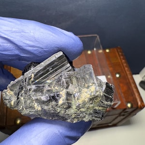Könnte beinhalten: Ein schwarzer, rauer und zerklüfteter Kristall mit einer glänzenden, reflektierenden Oberfläche. Der Kristall ist ein Cluster aus mehreren Spitzen und hat ein dunkles, fast undurchsichtiges Aussehen.