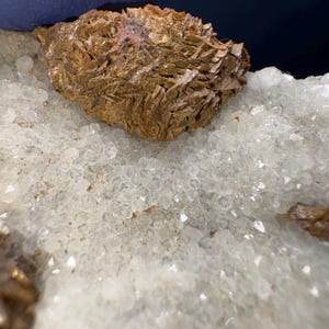 May include: A close-up of a brown, layered mineral specimen on a bed of white quartz crystals.