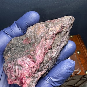 May include: A rough, gray rock with streaks of pink and red crystals. The rock is about the size of a hand.