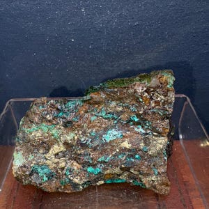 May include: A large, rough, brown rock with green and gold streaks. The rock is a sample of copper ore.