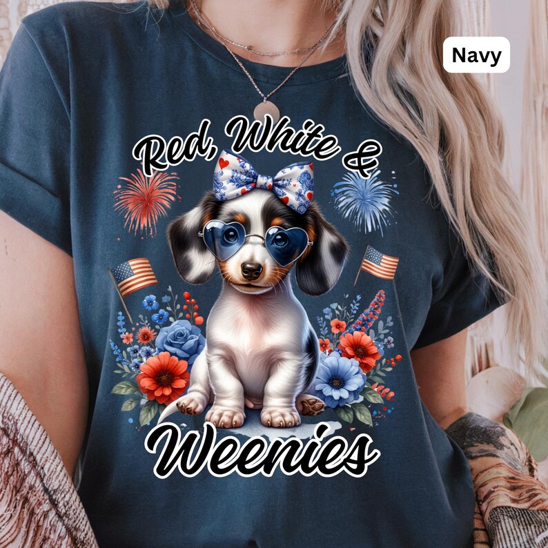 May include: Navy blue t-shirt featuring a dachshund wearing heart-shaped sunglasses and a bow. The shirt has the text "Red, White & Weenies" with fireworks and floral accents. The shirt also has the word "Navy" in the upper right corner.