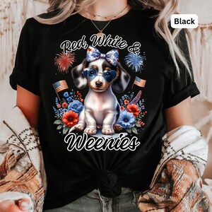 May include: Black t-shirt featuring a dachshund wearing heart-shaped sunglasses and a bow, surrounded by red, white, and blue flowers and fireworks. The text reads "Red, White & Weenies".