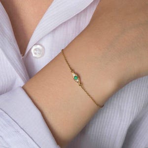 May include: A delicate gold chain bracelet with a small emerald green eye charm accented with tiny white diamonds.