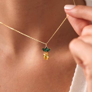 Op de afbeelding: Een gouden ketting met een ananas hanger. De ananas is gemaakt van gele en groene kristallen.