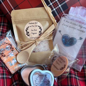 Puede incluir: Un set de regalo con productos para el baño y el cuerpo, que incluye una vela en forma de corazón, jabón y sales de baño. Los productos están etiquetados como "Iron Brew Fragrance" y se presentan con una cuchara de madera y rafia.