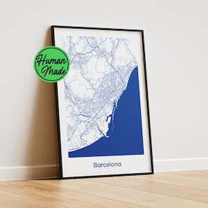 May include: A framed vertical map print of Barcelona featuring a white background with blue street lines and a solid blue coastal area. The text "Barcelona" is printed in blue at the bottom. A green circular badge with "Human Made" is visible.