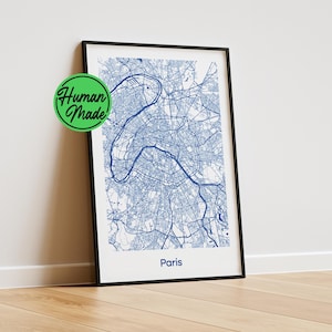 Op de afbeelding: Een ingelijste verticale wandkunstprint met een gedetailleerde blauwe stadsplattegrond van Parijs op een witte achtergrond. De kaart toont complexe stratenpatronen en de rivier de Seine. Het woord Paris staat onderaan in het blauw. Een groen rond Human Made logo.