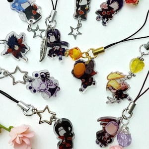 May include: A collection of anime-style character charms with black cords and star-shaped clasps. The charms feature various characters in vibrant colors, with some including additional decorative elements like feathers and beads. The background is white with pink flowers.